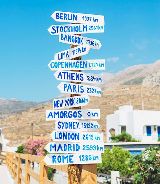 Blue and white signs in Amorgos pointing to various world capitals and their distances